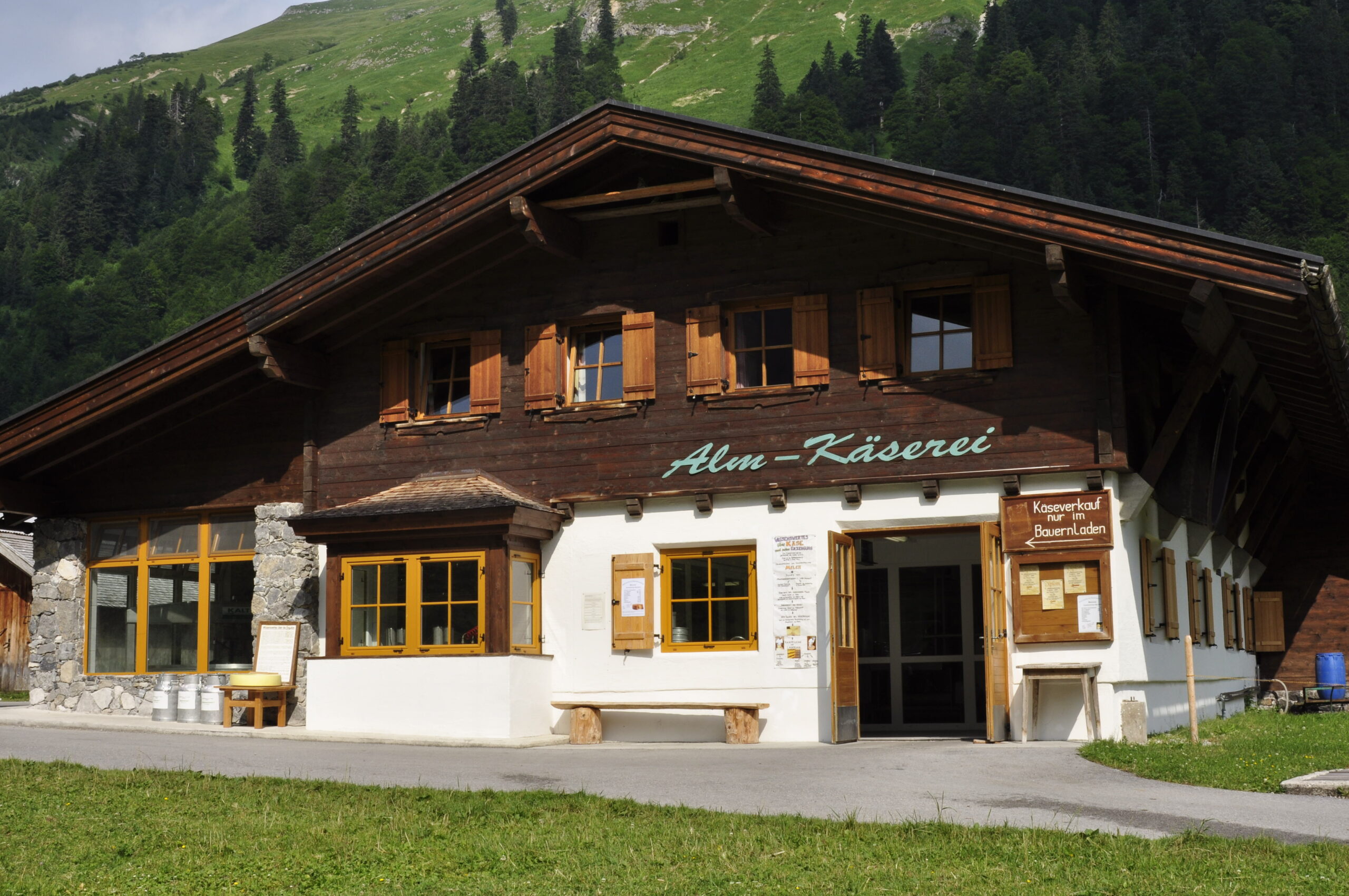 Ein hölzernes Almkäsereigebäude mit der Aufschrift "Alm-Käserei" an der Fassade steht in den grünen Bergen unter freiem Himmel - Teil der historischen Käserei auf der Engalm.