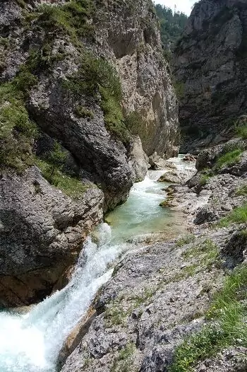 Ein schmaler Fluss mit schnell fließendem Wasser fließt zwischen felsigen Klippen und steilen, grasbewachsenen Hängen in der Berglandschaft der Gleirschklamm.
