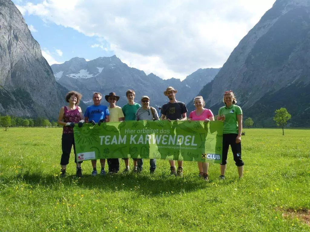 Eine Gruppe von acht Personen steht auf der Wiese am Großen Ahornboden vor den Bergen und hält ein grünes Transparent mit der Aufschrift "Hier arbeitet das TEAM KARWENDEL".