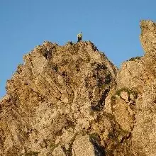 Eine Person steht auf einem zerklüfteten, felsigen Gipfel am berühmten Tiroler Adlerweg und sonnt sich unter einem strahlend blauen Himmel.