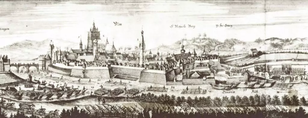 Schwarz-weiße historische Illustration einer ummauerten Stadt mit Schlössern, Kirchen und umliegenden Truppen; im Hintergrund sind beschriftete Wahrzeichen, Landschaftsmerkmale und Hinweise auf die Flößerei zu sehen.