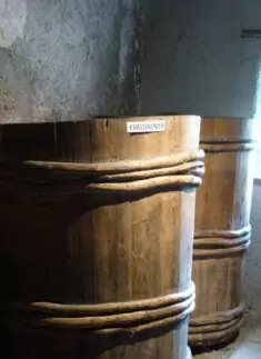 Zwei große Gärbottiche aus Holz, die mit dicken Seilen verstärkt sind, stehen bei schwachem Licht nebeneinander an einer strukturierten Wand. Ihr robuster Werkstoff verkörpert traditionelle Handwerkskunst.