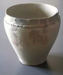 Ein weißer, alter Keramiktopf mit sichtbaren Rissen und ausgebesserten Stellen steht auf einer glatten Fläche, die an die in der Saline Hall ausgestellten Artefakte erinnert.