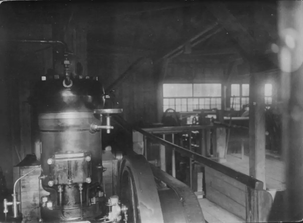 Eine alte Dampflokomotive in einem hölzernen Industriegebäude mit sichtbaren Maschinenteilen und Balken unter natürlichem Fensterlicht erinnert an den historischen Charme einer Bremsbergbahnanlage.