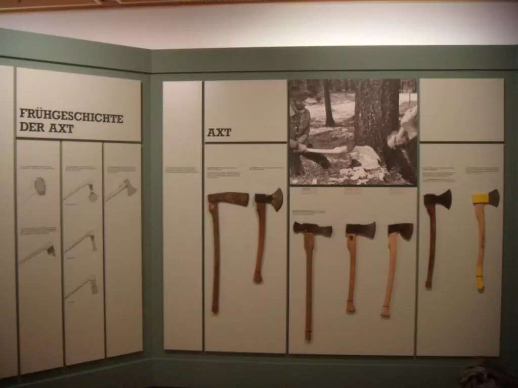 Exponat zur frühen Geschichte der Äxte, mit verschiedenen Holzerwerkzeugen an der Wand, mit beschreibendem Text und einem Schwarz-Weiß-Foto von Äxten im Gebrauch.
