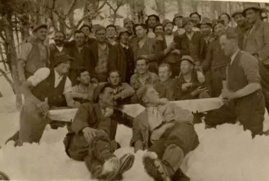 Eine Gruppe von Männern posiert gemeinsam im Freien im Schnee, wobei einige stehen und andere sitzen oder sich vorne anlehnen.