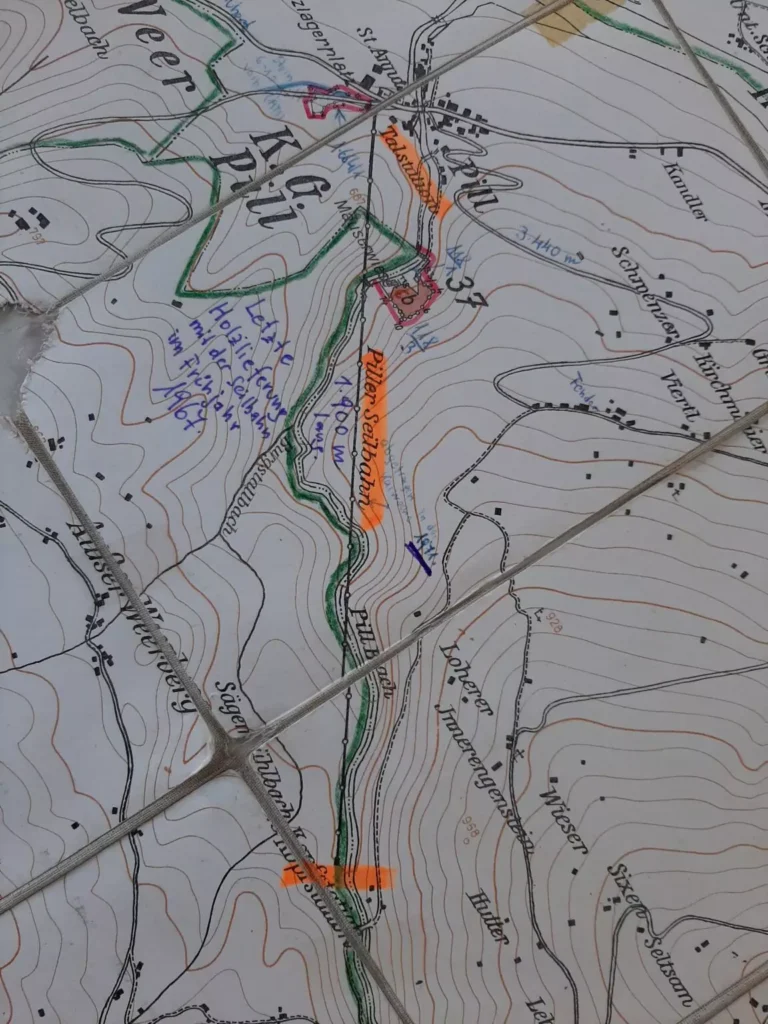 Eine Nahaufnahme einer topografischen Karte auf Kacheln mit verschiedenen farbigen handschriftlichen Routenmarkierungen und Notizen, die Höhenlinien, Wege und Ortsnamen zeigen.