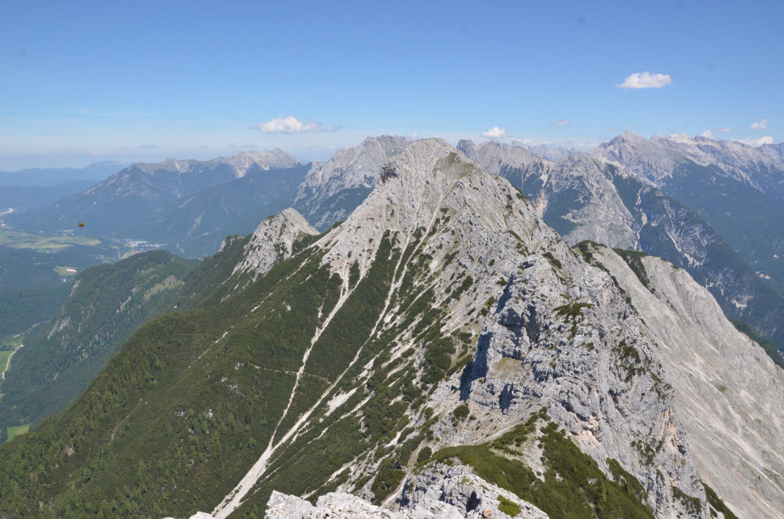 Gebirgskamm mit felsigen Gipfeln und grünen Hängen unter einem klaren blauen Himmel, mit der beeindruckenden Arnspitzkette, mit entfernten Bergen im Hintergrund.