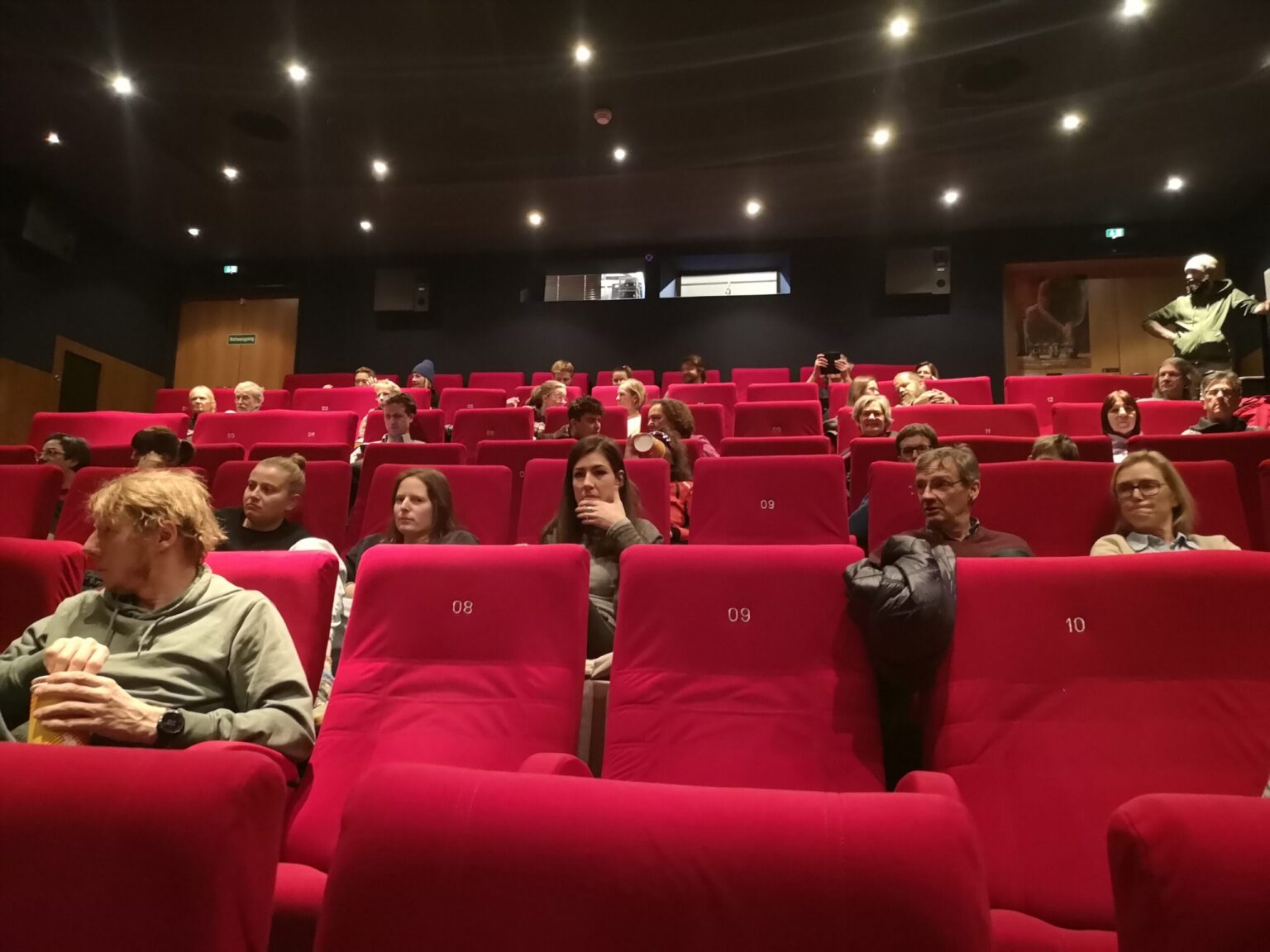 Die Zuschauer sitzen in roten Samtsesseln in einem schwach beleuchteten Kinosaal beim Nature Filmfestival on Tour, mehrere Reihen sind teilweise gefüllt und eine Person steht ganz hinten.