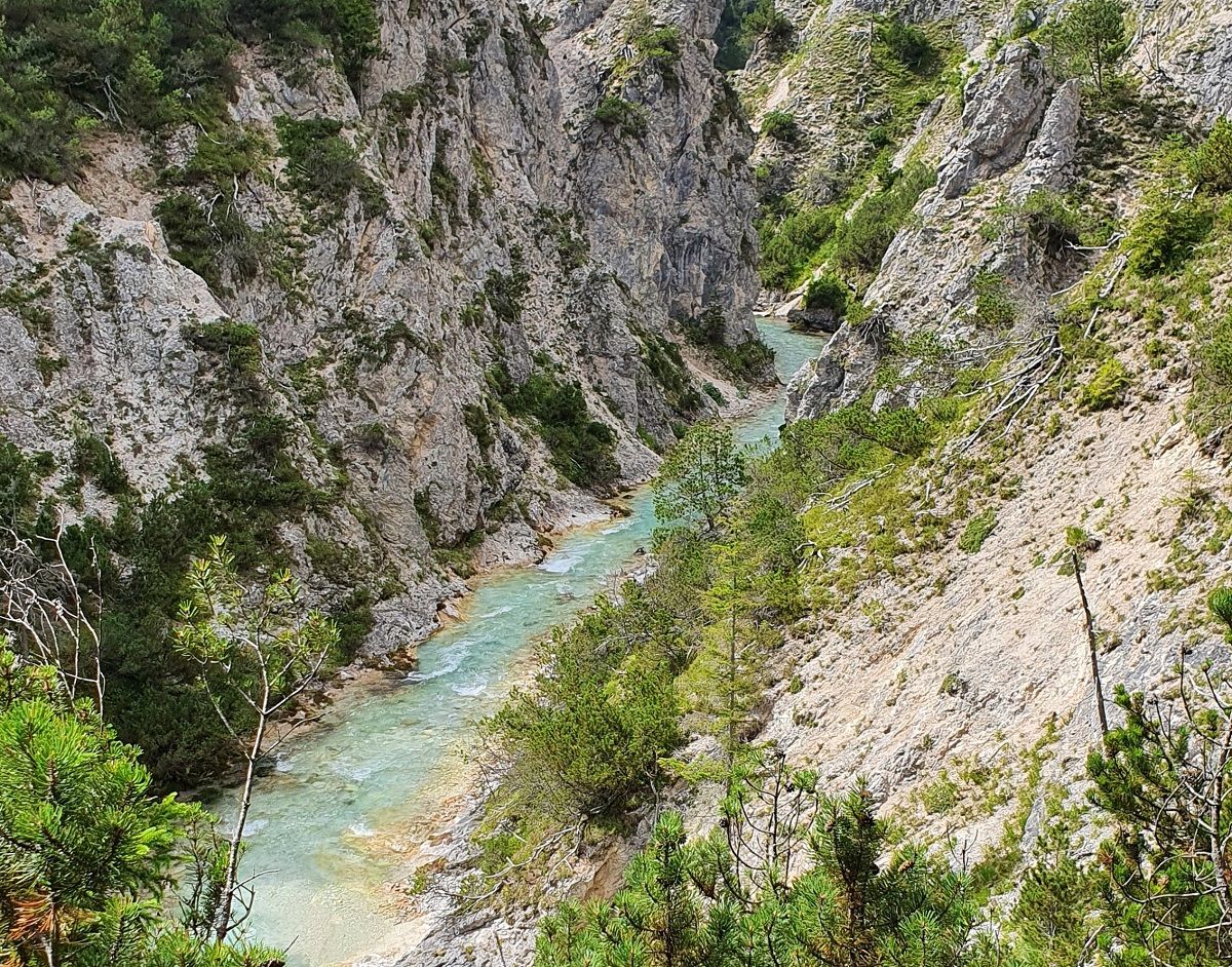 Ein schmaler türkisfarbener Fluss schlängelt sich durch die felsige Gleirschklamm, eingerahmt von steilen Felsen und spärlicher grüner Vegetation.