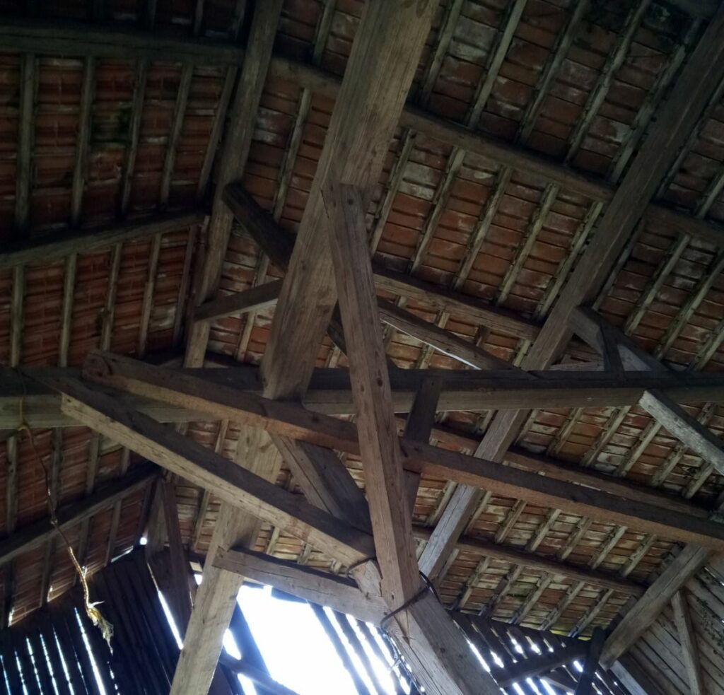 Holzbalken (Holz) tragen ein schräges Dach mit roten Ziegeln, das von unten gesehen etwas Licht durch die Lücken in der Struktur hereinlässt - ein Zeugnis für diesen vielseitigen Werkstoff.