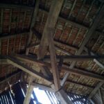 Holzbalken (Holz) tragen ein schräges Dach mit roten Ziegeln, das von unten gesehen etwas Licht durch die Lücken in der Struktur hereinlässt - ein Zeugnis für diesen vielseitigen Werkstoff.