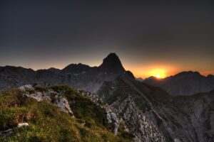 Die Sonne geht hinter den schroffen Gipfeln der Nordkette unter und wirft Schatten auf felsiges Gelände und grasbewachsene Hänge - und fängt das Wesen von Leben im Gebirge ein.