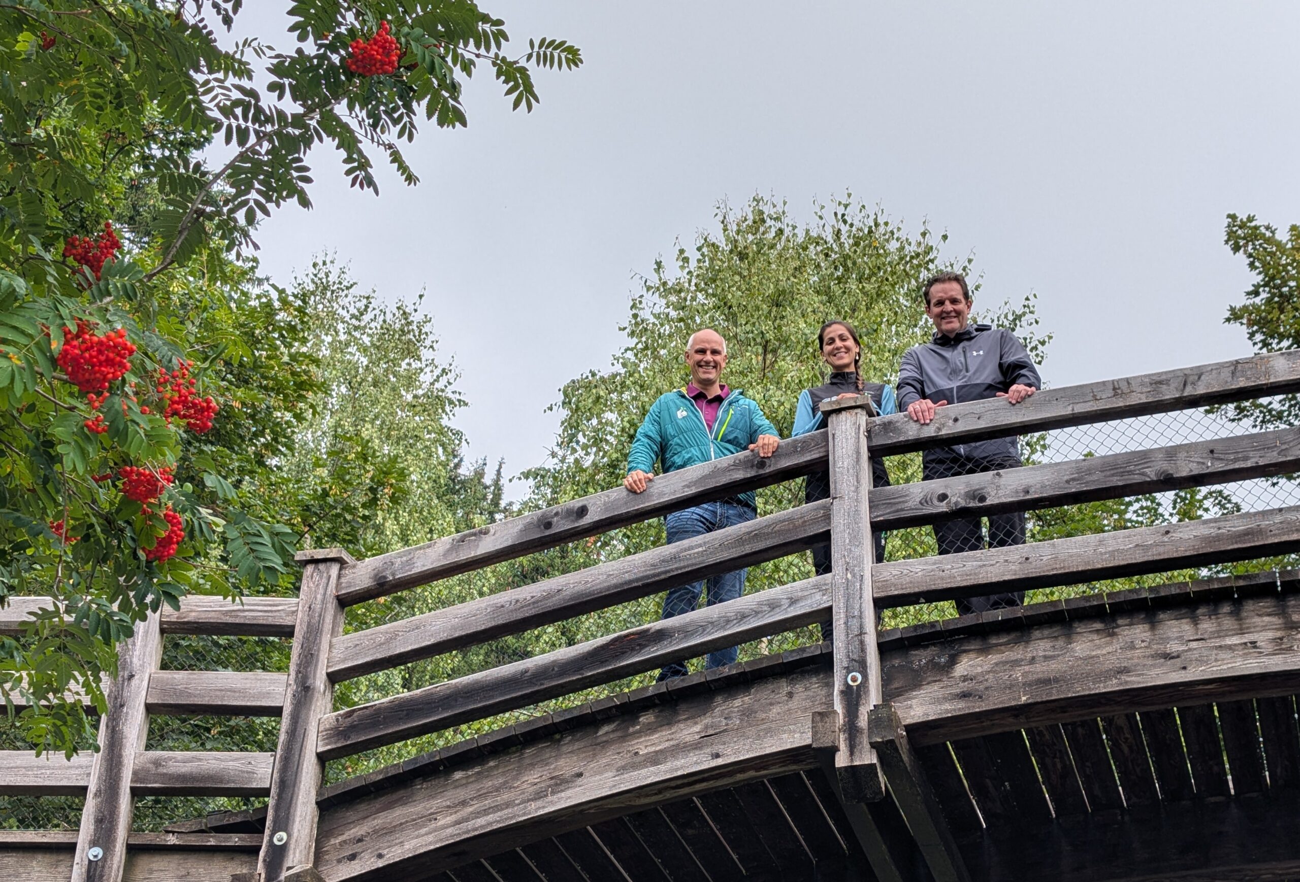 Foto von LR René Zumtobel, Digital Rangerin Iris Trikha und GF Anton Heufelder (beide vom Naturpark Karwendel) auf einer Holzbrücke am Halltal Eingang.