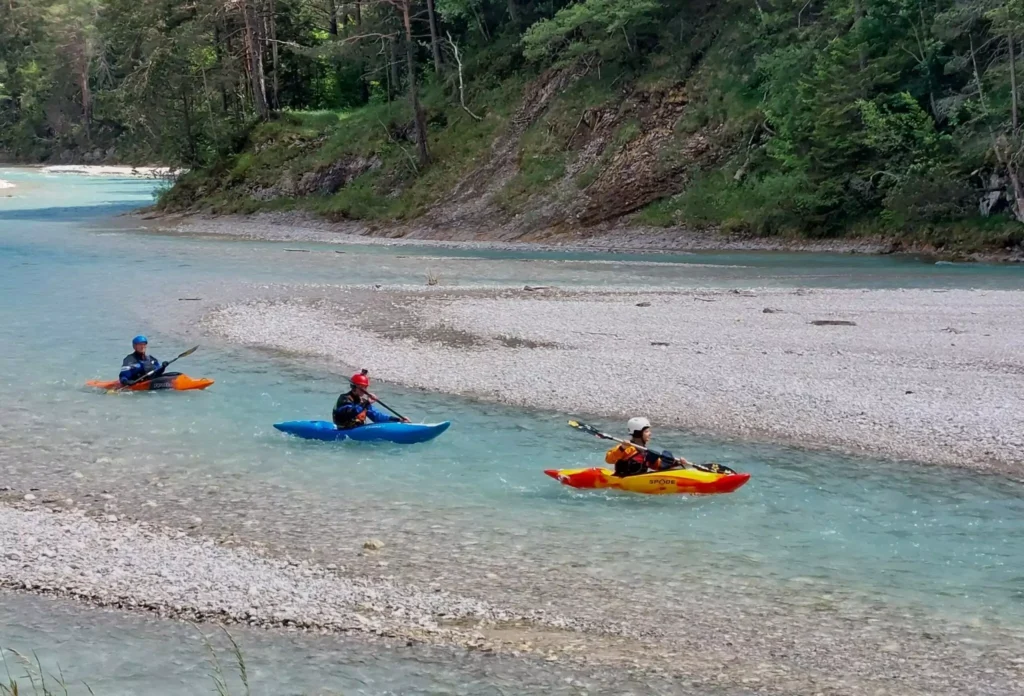 Drei Personen im Kajak auf einem seichten, klaren Fluss, umgeben von felsigen Ufern und bewaldeten Hügeln - ideal für beeindruckende Foto-/ Filmaufnahmen & Drohnen-Perspektiven.