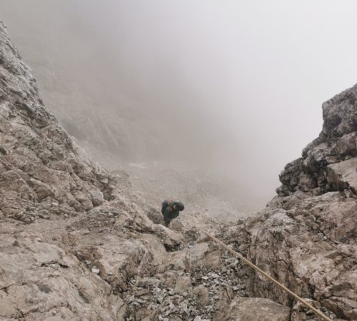 Eine Person trotzt den nebligen, schlecht sichtbaren Bedingungen beim Klettern im Karwendel und klettert mit Hilfe eines Seils einen felsigen, steilen Berghang hinauf.