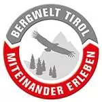 Kreisförmiges Logo mit dem Schriftzug "Bergwelt Tirol Miteinander Erleben", das einen Adler zeigt, der über Berge und Bäume schwebt und den Geist der Partnerschaft und Einigkeit zwischen Naturliebhabern und Partnern symbolisiert.