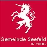 Weißes Einhorn auf Hinterbeinen über dem Schriftzug "Gemeinde Seefeld in Tirol" auf rotem Grund, das den Geist der Gemeinde als stolzer Partner in der Einheit symbolisiert.