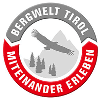 Logo Bergwelt Tirol Kreisförmiges Logo mit einem fliegenden Adler, einem Berg und Bäumen in der Mitte. Der graue Text lautet "Bergwelt Tirol" und der rote Text "Miteinander Erleben". Perfekt für Mountainbiken Karwendel-Abenteuer.