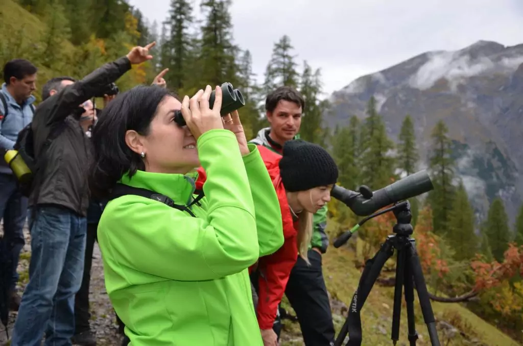 Bei einer Naturführung beobachtet eine Gruppe von Menschen auf einem Bergpfad mit Fernglas und Spektiv etwas in der Ferne.