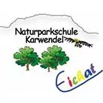 Logo mit dem Text "Naturparkschule Karwendel", zwei Bäumen, einem fliegenden Vogel, einem Bergumriss und "EicHat" in bunten Buchstaben unten rechts, die die Schule als stolzen Partner der Naturerziehung hervorheben.