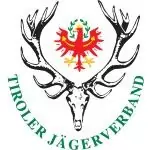 Logo mit einem rot-gelben Adler über einem Hirschschädel mit Geweih, umgeben vom Schriftzug "Tiroler Jägerverband" in grüner Schrift, als Symbol für den Zusammenhalt der Jäger und ihrer Partner in der Tradition.