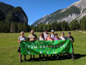 Acht Personen stehen im Freien auf einer Wiese vor Bergen und Bäumen und halten ein grünes Transparent mit der Aufschrift "TEAM KARWENDEL".