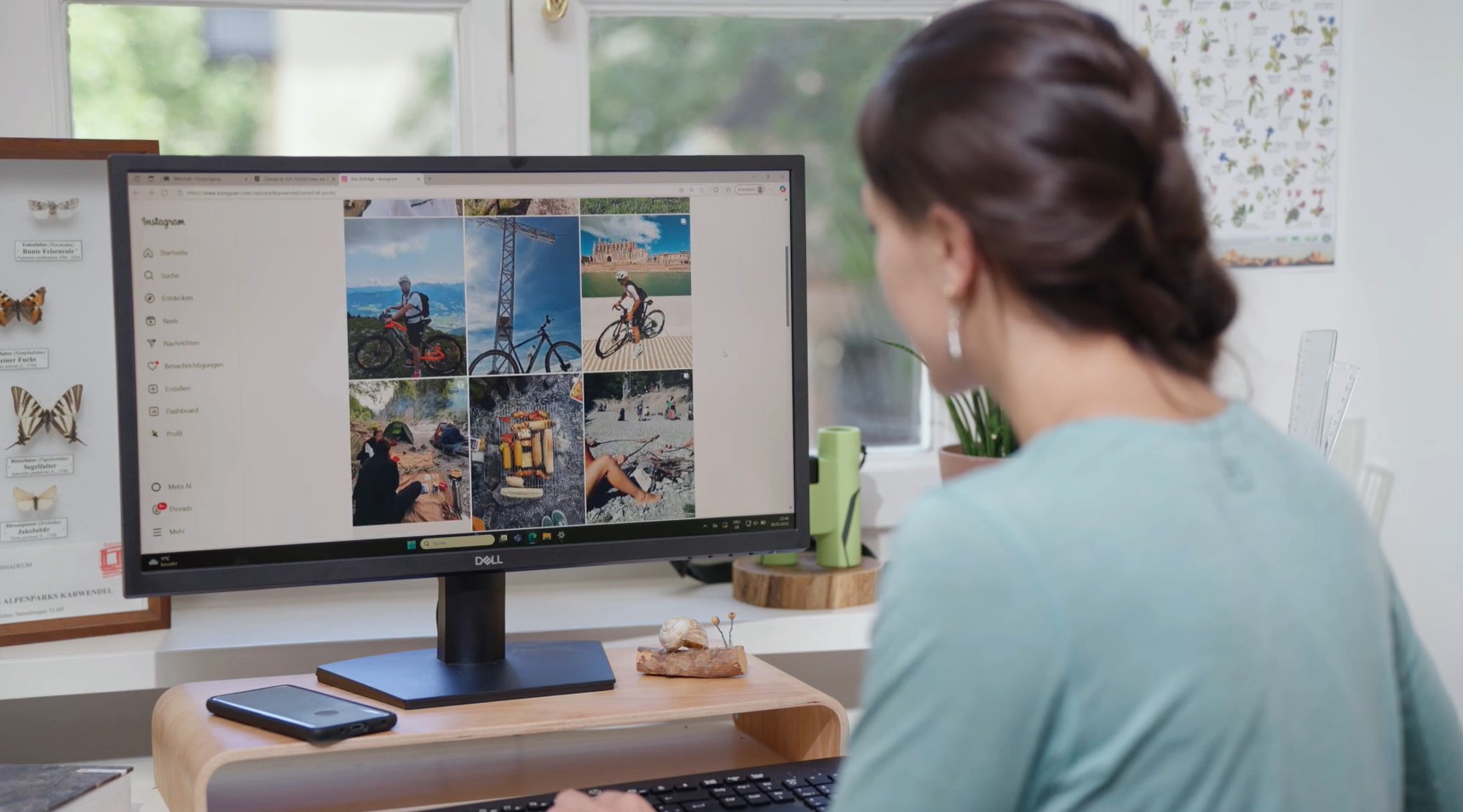 Eine Frau sitzt an einem Schreibtisch und schaut auf einen Computermonitor, auf dem ein Instagram-Fotoraster mit Outdoor- und Reisebildern zu sehen ist, darunter auch Bilder von Abenteuern als Naturpark-Rangerin.