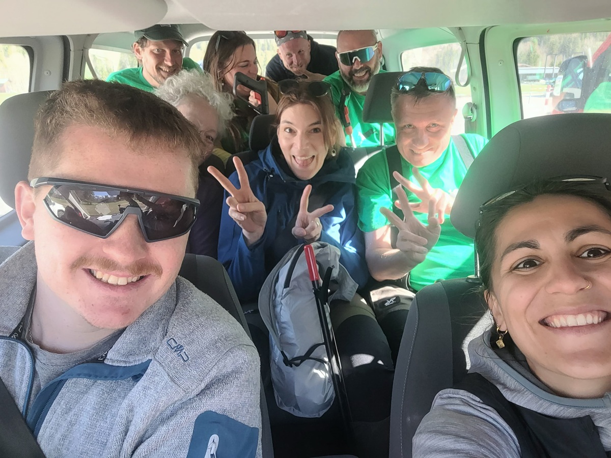 Eine Gruppe von neun Personen sitzt nach einer Müllsammelaktion in den Karwendeltälern in der Nähe des Achensees eng beieinander und lächelt in die Kamera; einige machen mit ihren Händen Friedenszeichen.