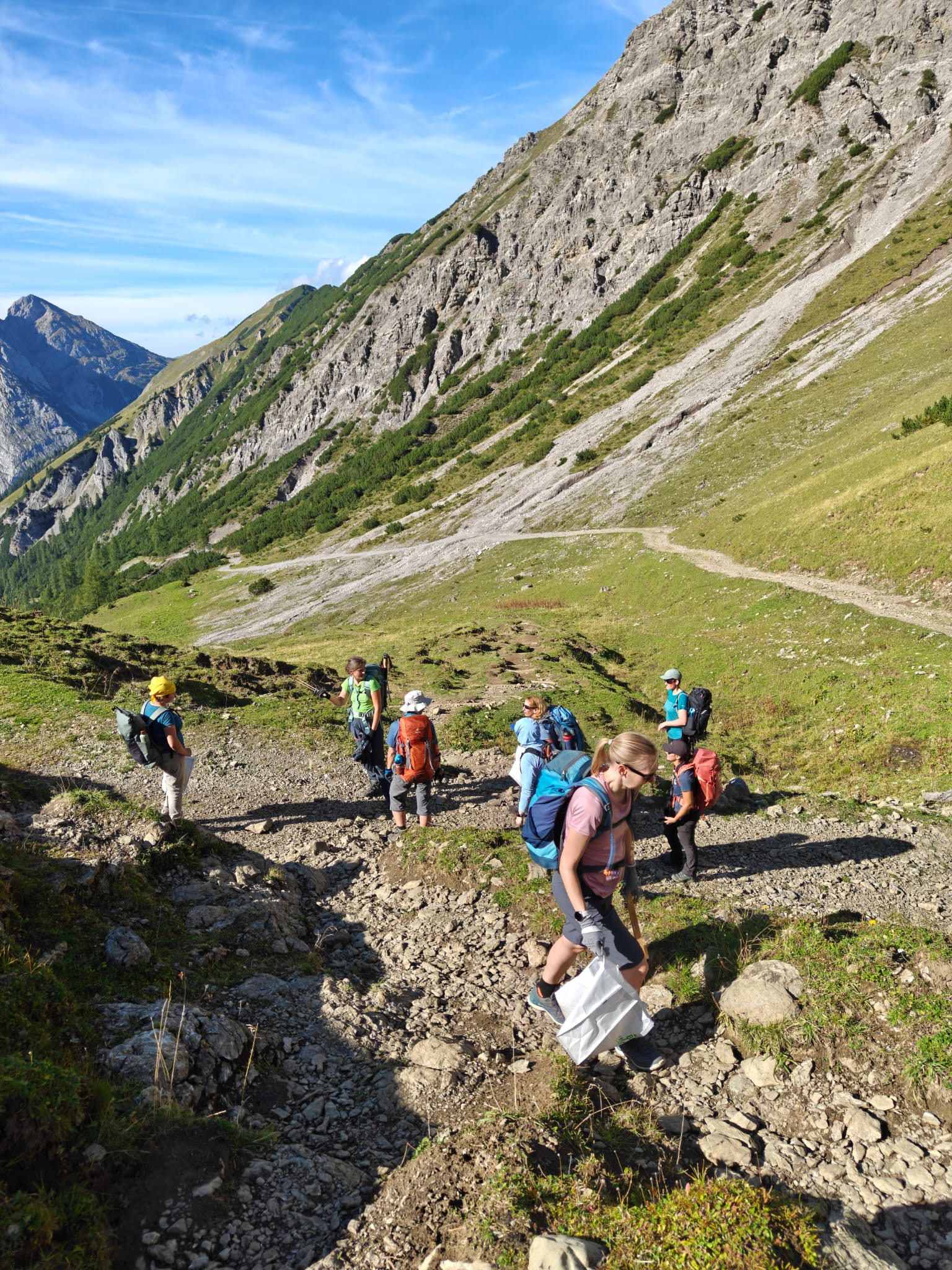 Eine Gruppe von Wanderern mit Rucksäcken, die auf einem felsigen Bergpfad in der Nähe der Walderalmteiche hinuntergehen.