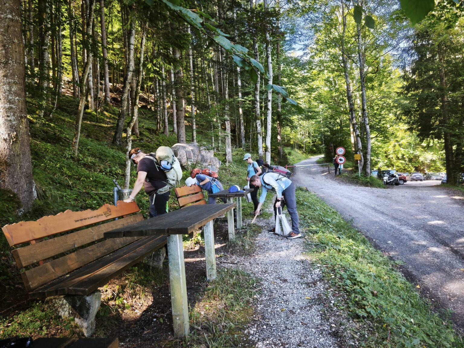 Drei Wanderer mit Rucksäcken stehen neben einer Holzbank und einem Tisch auf einem Waldweg in der Nähe der Walderalmteiche.